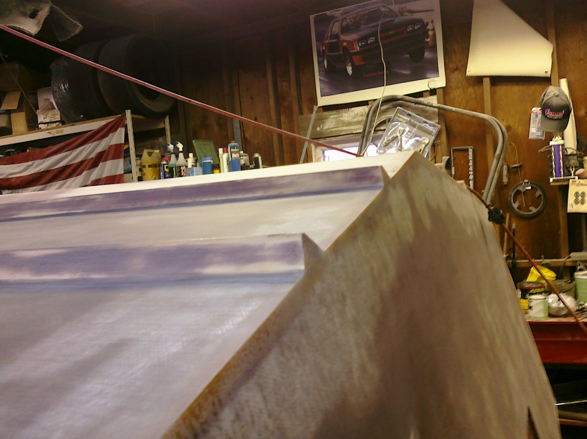 Looking down the faired hull bottom, a Fox Body Mustang poster and American flag on the garage wall