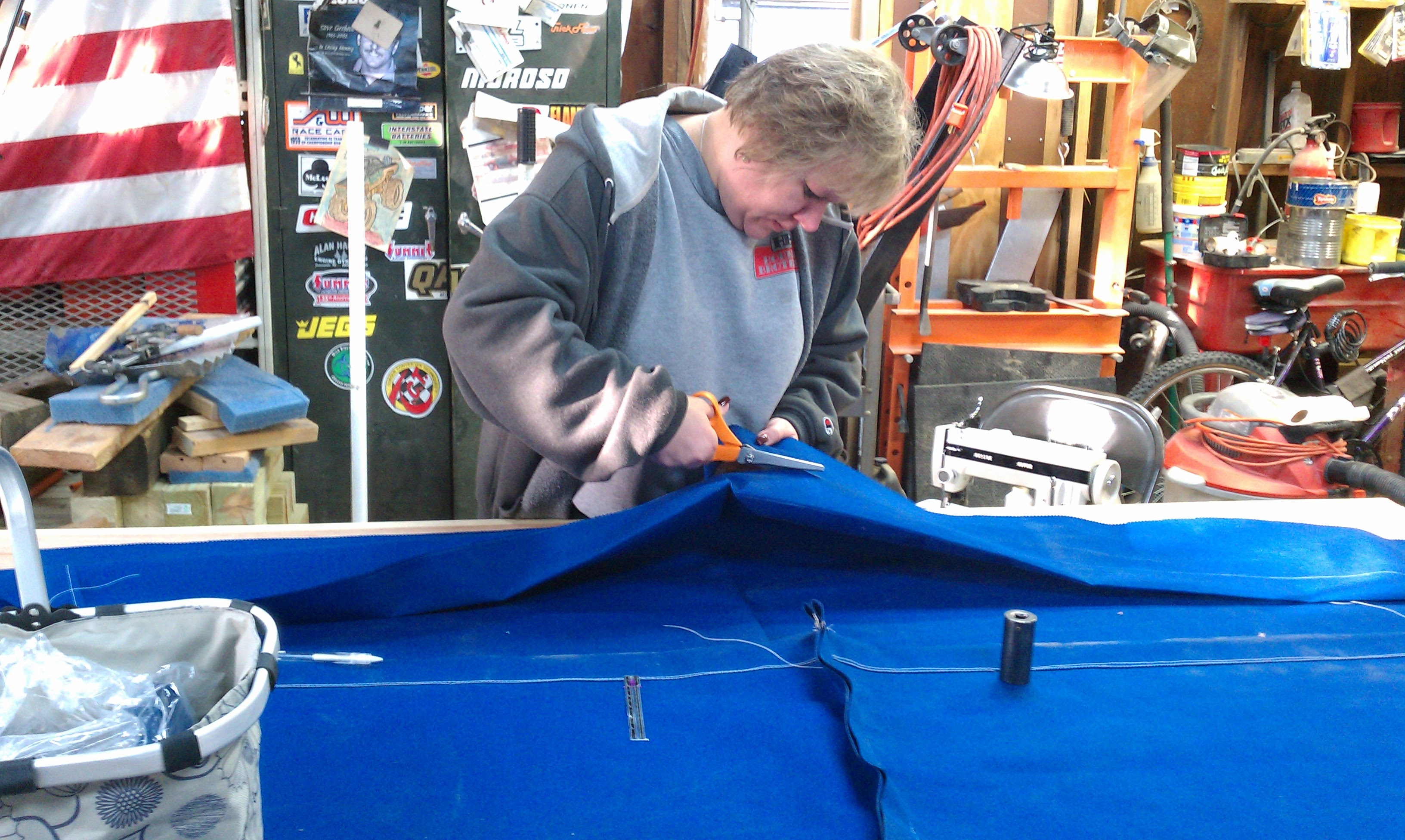 Joanne cutting the blue canvas cover at the workbench, racing stickers on the toolbox behind her