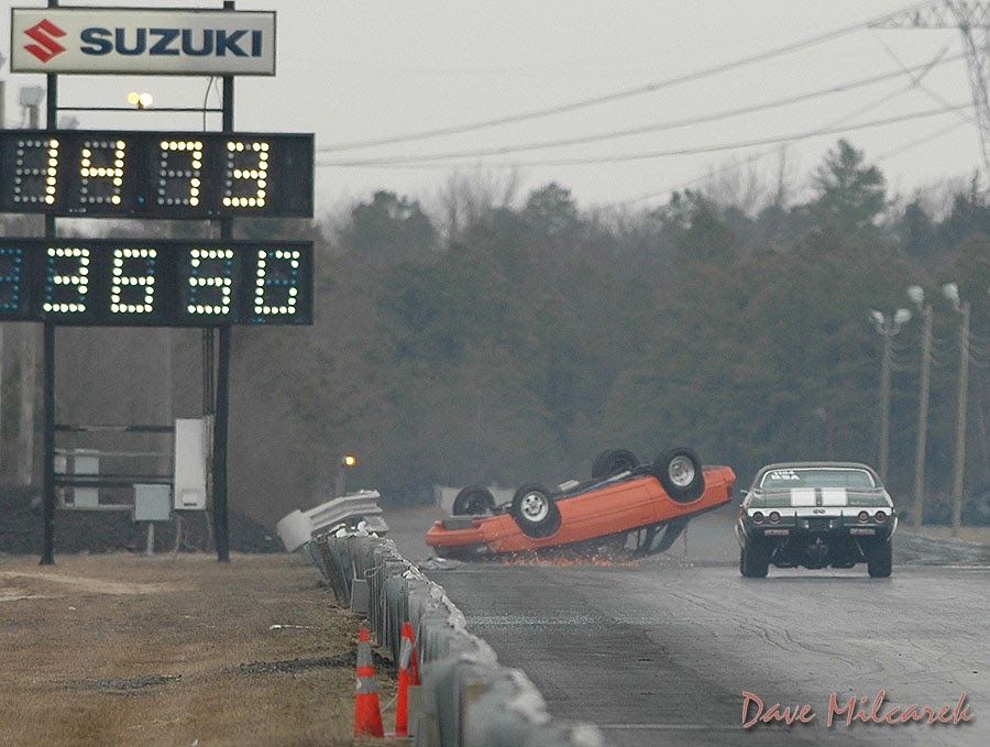 Wide shot - car inverted at guardrail, timing board in frame