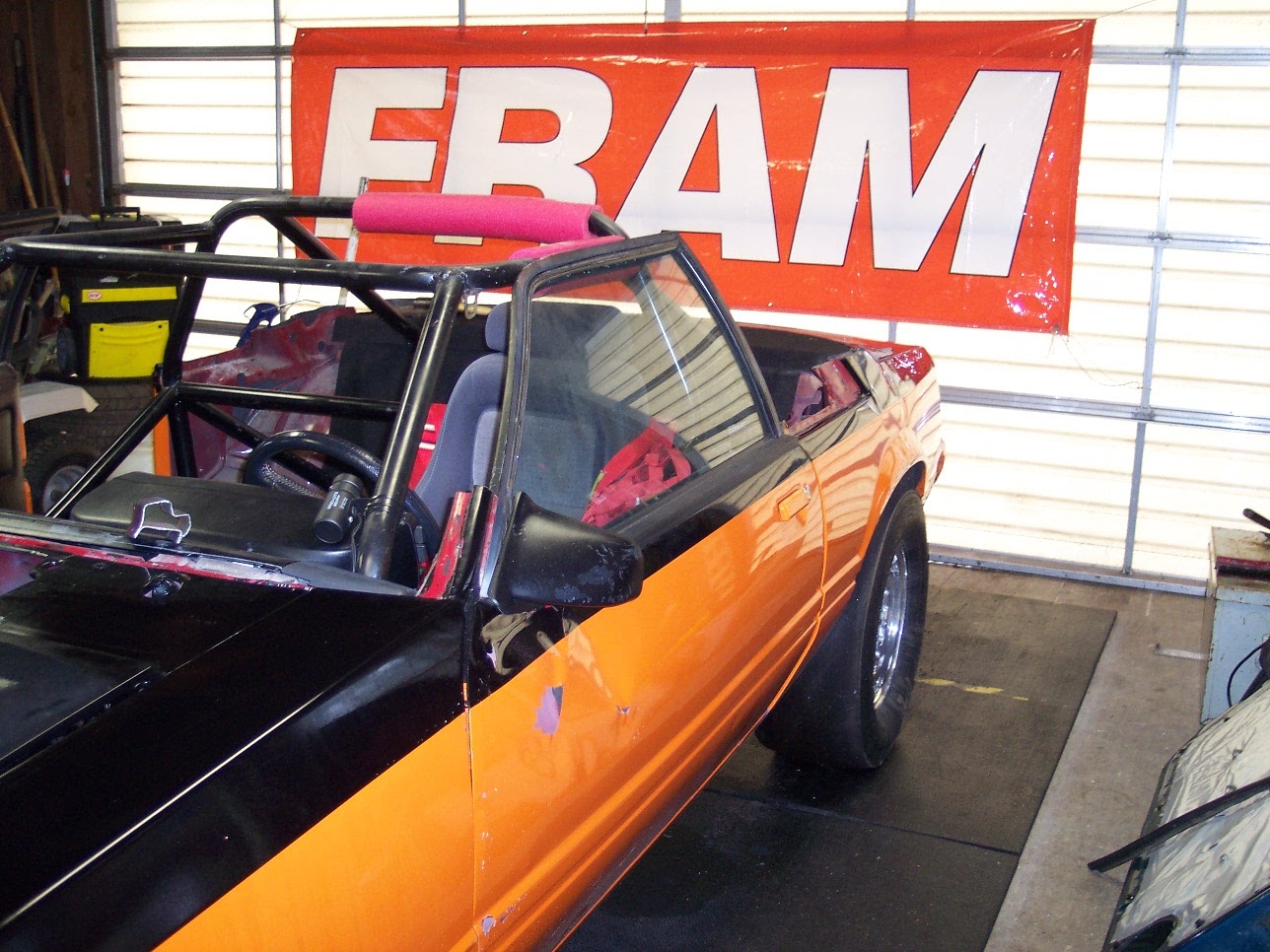 Car roofless in the garage, FRAM banner behind
